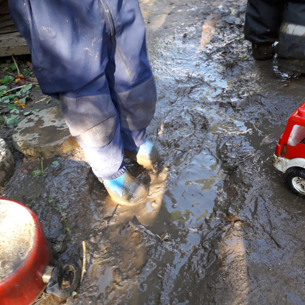 Ein Kind steht mit Regenstiefeln in einer matschigen Pfütze
