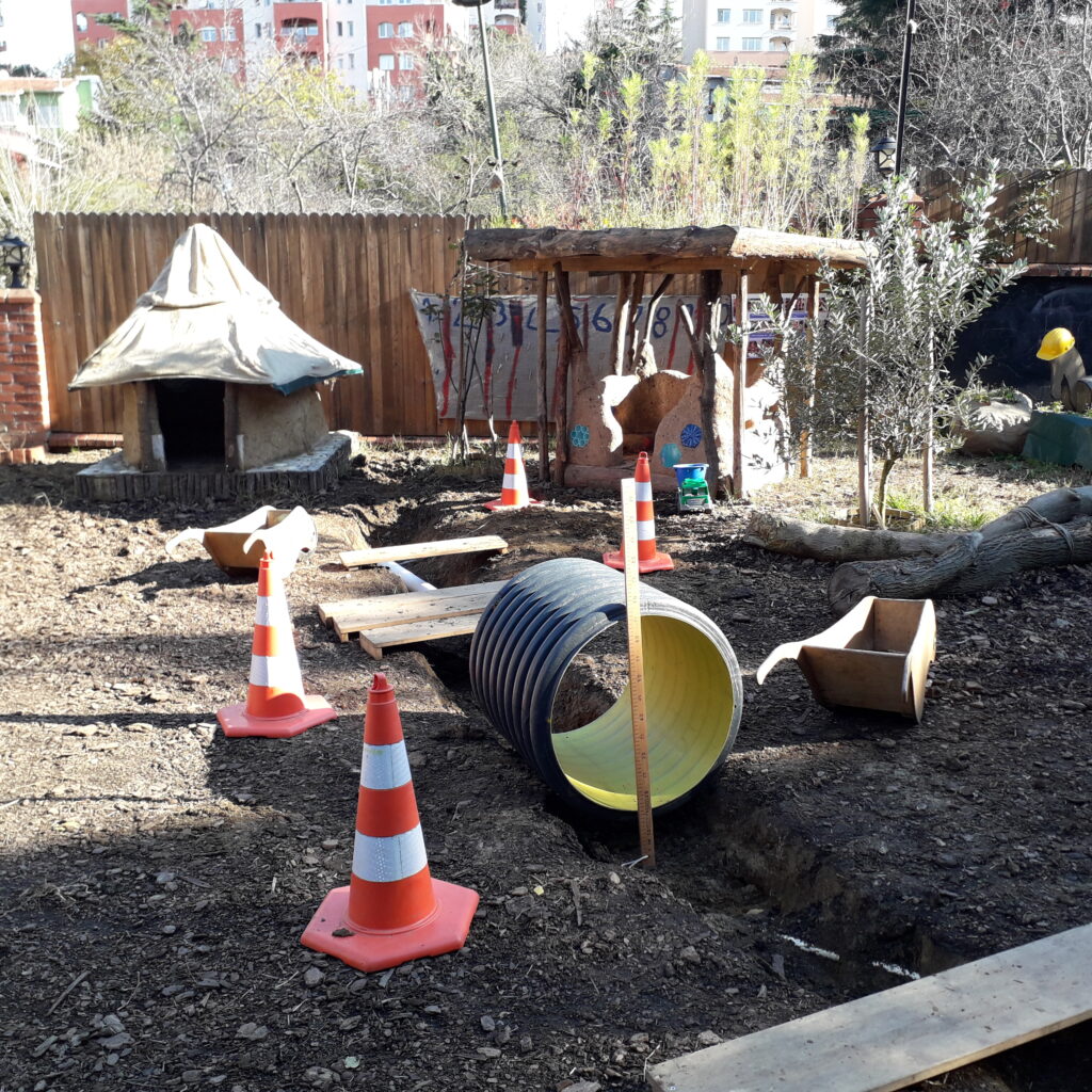 Der EBİ Garten mit losen Brettern, einem grossen Rohr und Verkehrszeichen als Spielmaterialien