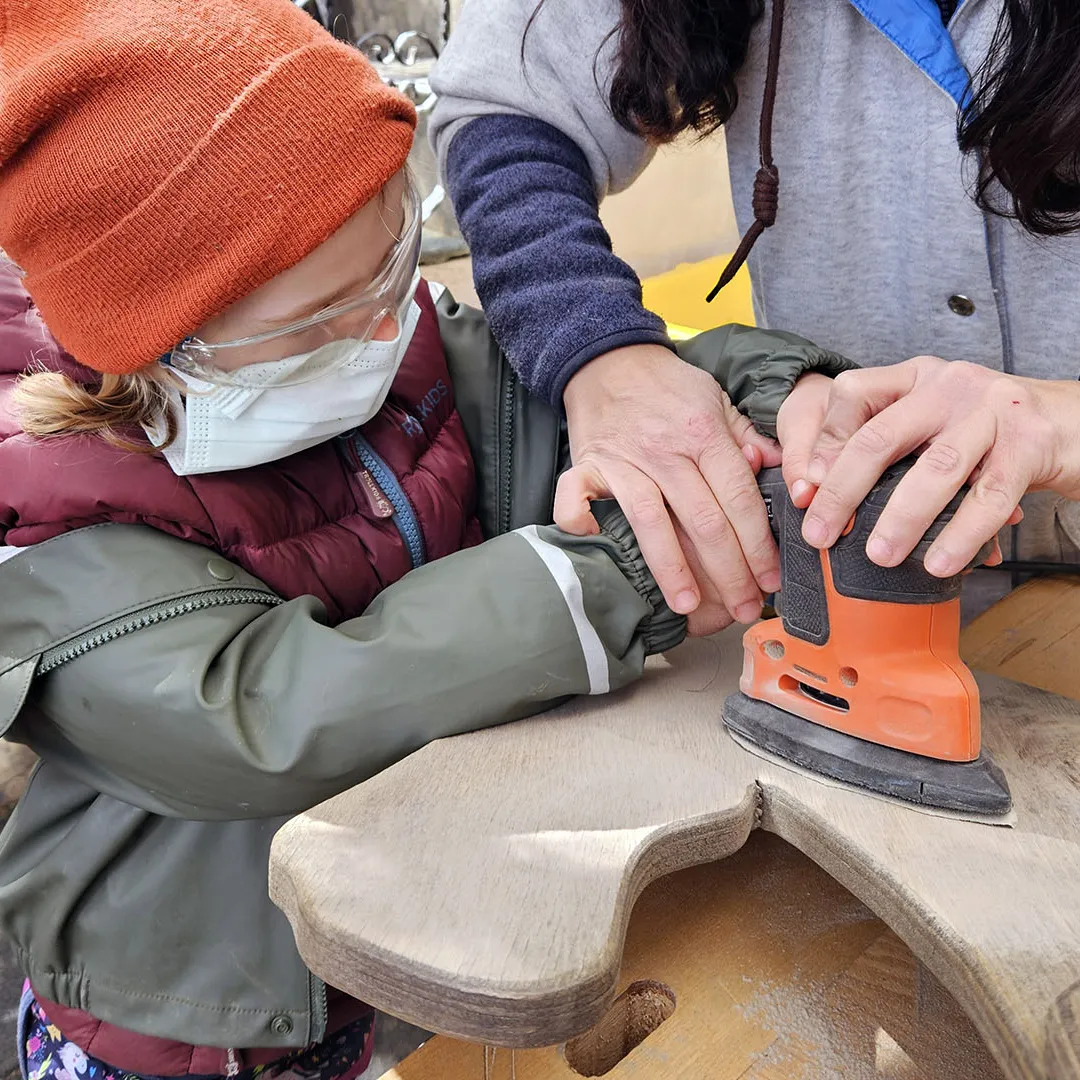 Ein Kind und die Begleiterin schleifen das Holzpferd glatt