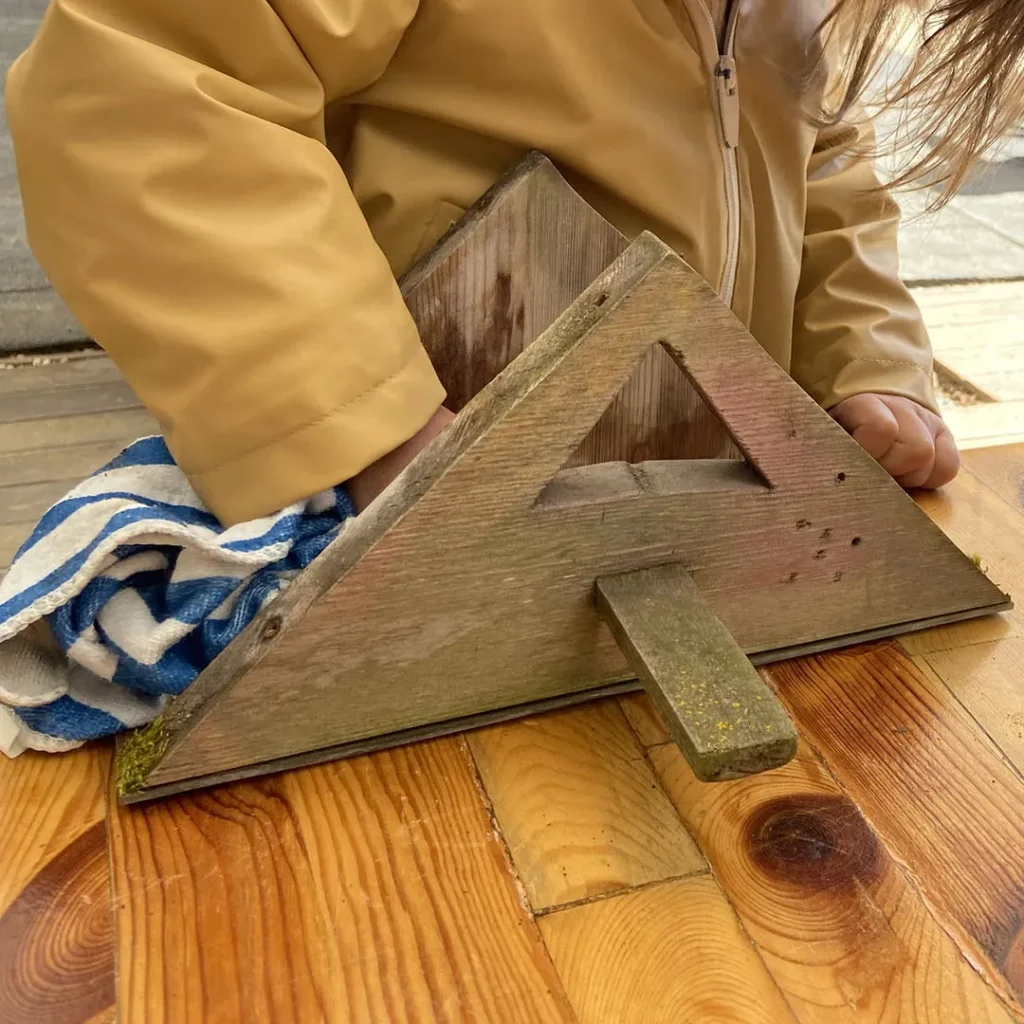 Ein Kind reinigt das Vogelhaus mit einem Lappen