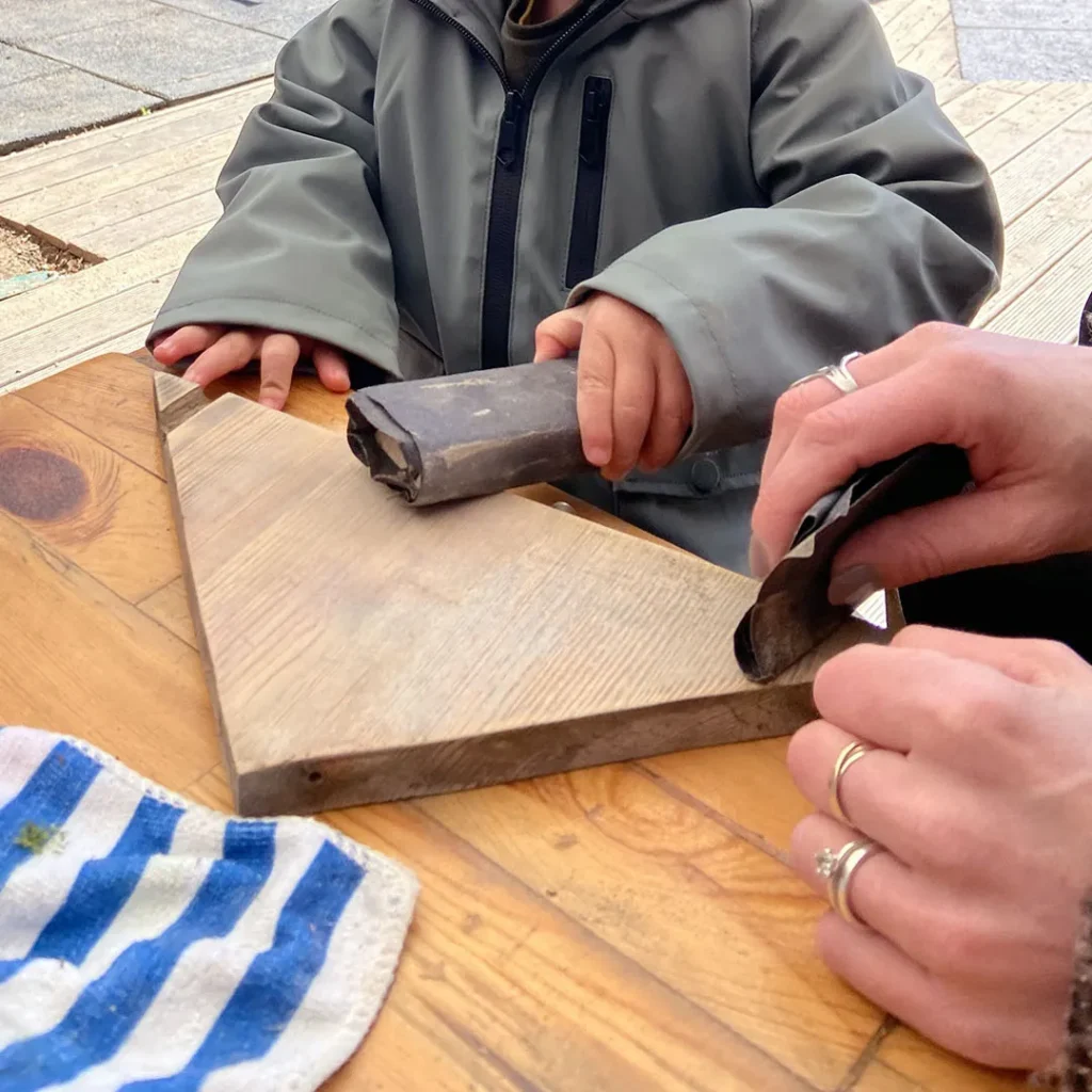 Ein Kind schmirgelt die Holzteile des Vogelhauses glatt