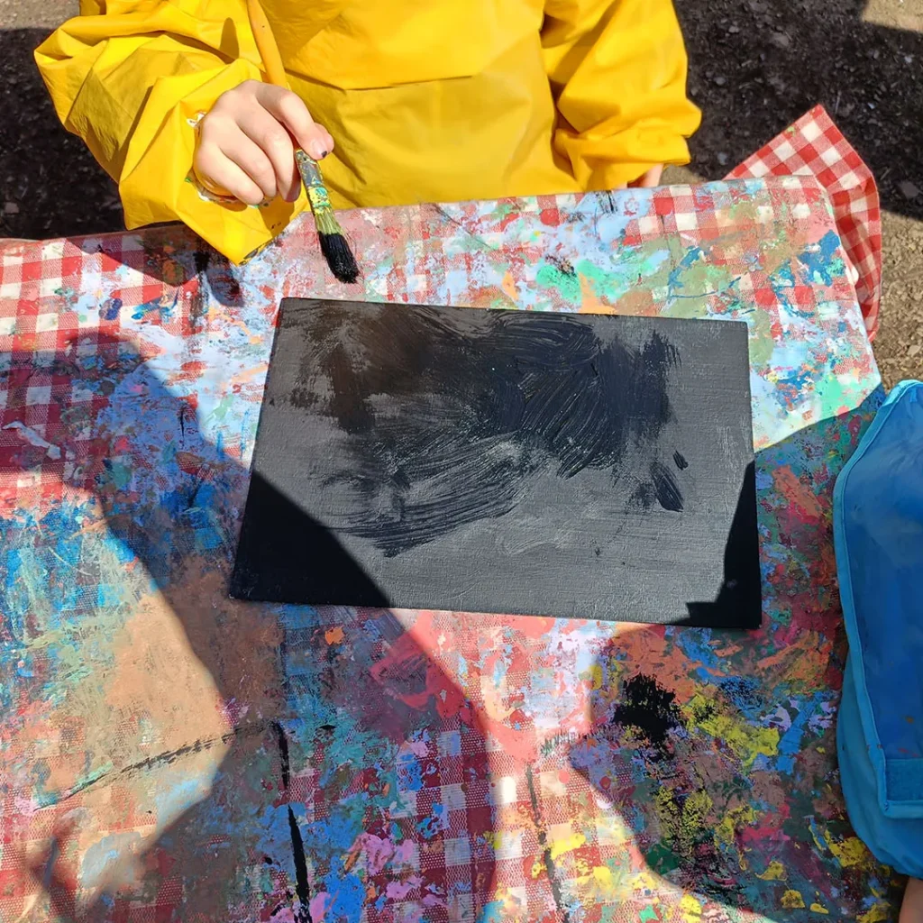 Ein Kind streicht die Tafel mit schwarzer Farbe an