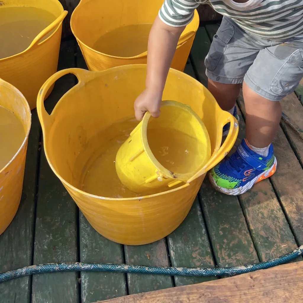 Kind schöpft Wasser aus einem Eimer