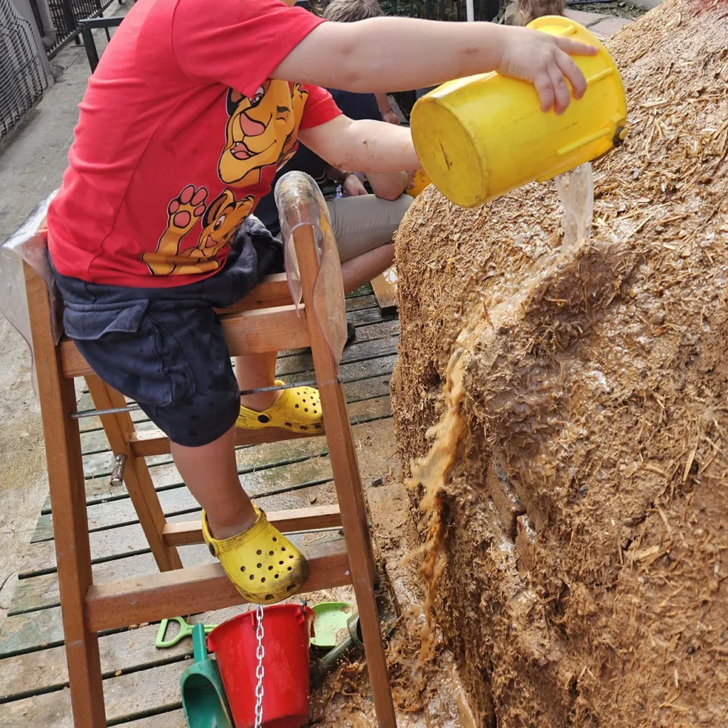 Ein Kind giesst Wasser über die Lehmkuppel