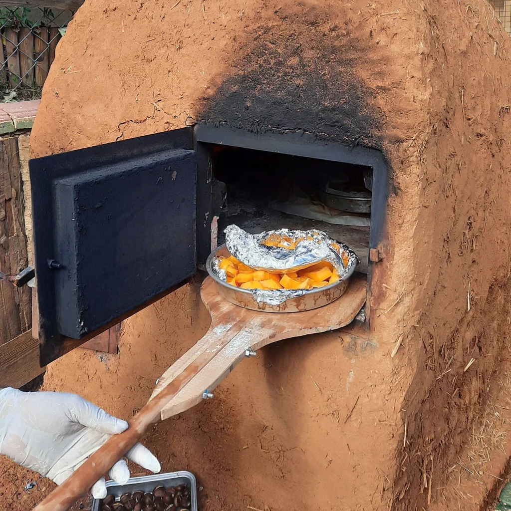 Eine Mitarbeiterin schiebt mit einem grossen Holzschieber ein Blech mit Kürbissstücken in den Erdofen hinein
