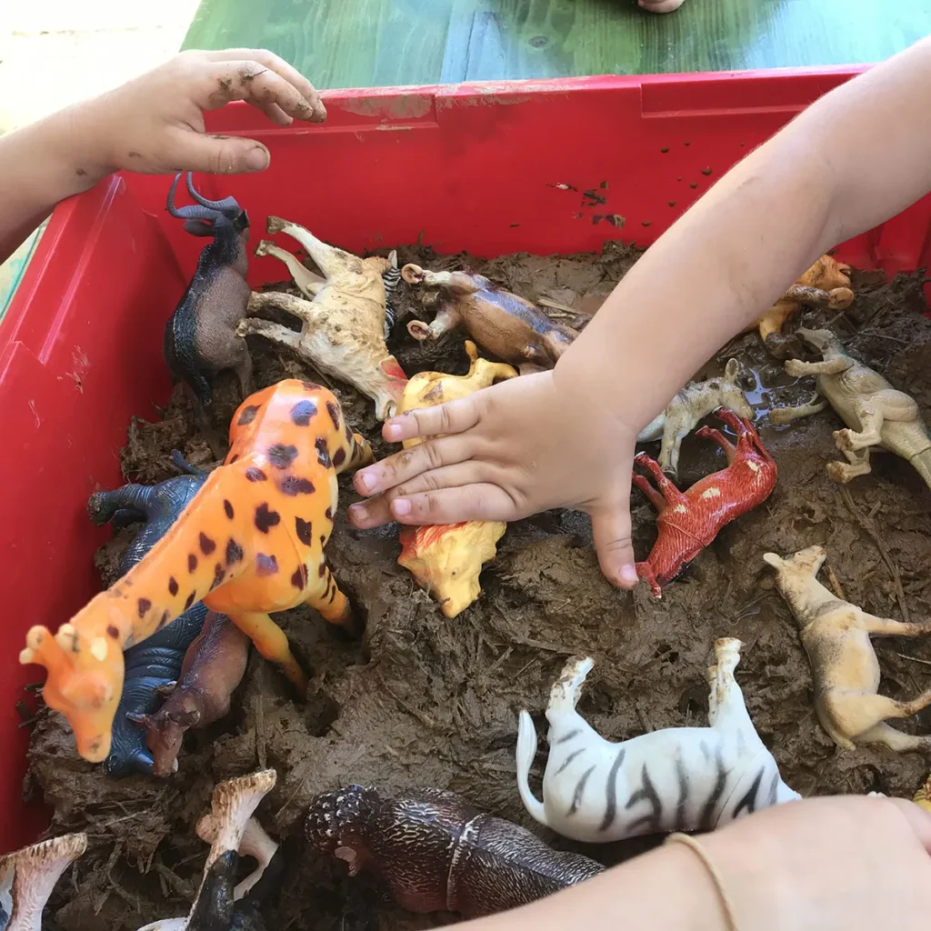 Kinder spielen mit Plastiktieren in einer Wanne gefüllt mit feuchter Lehmerde
